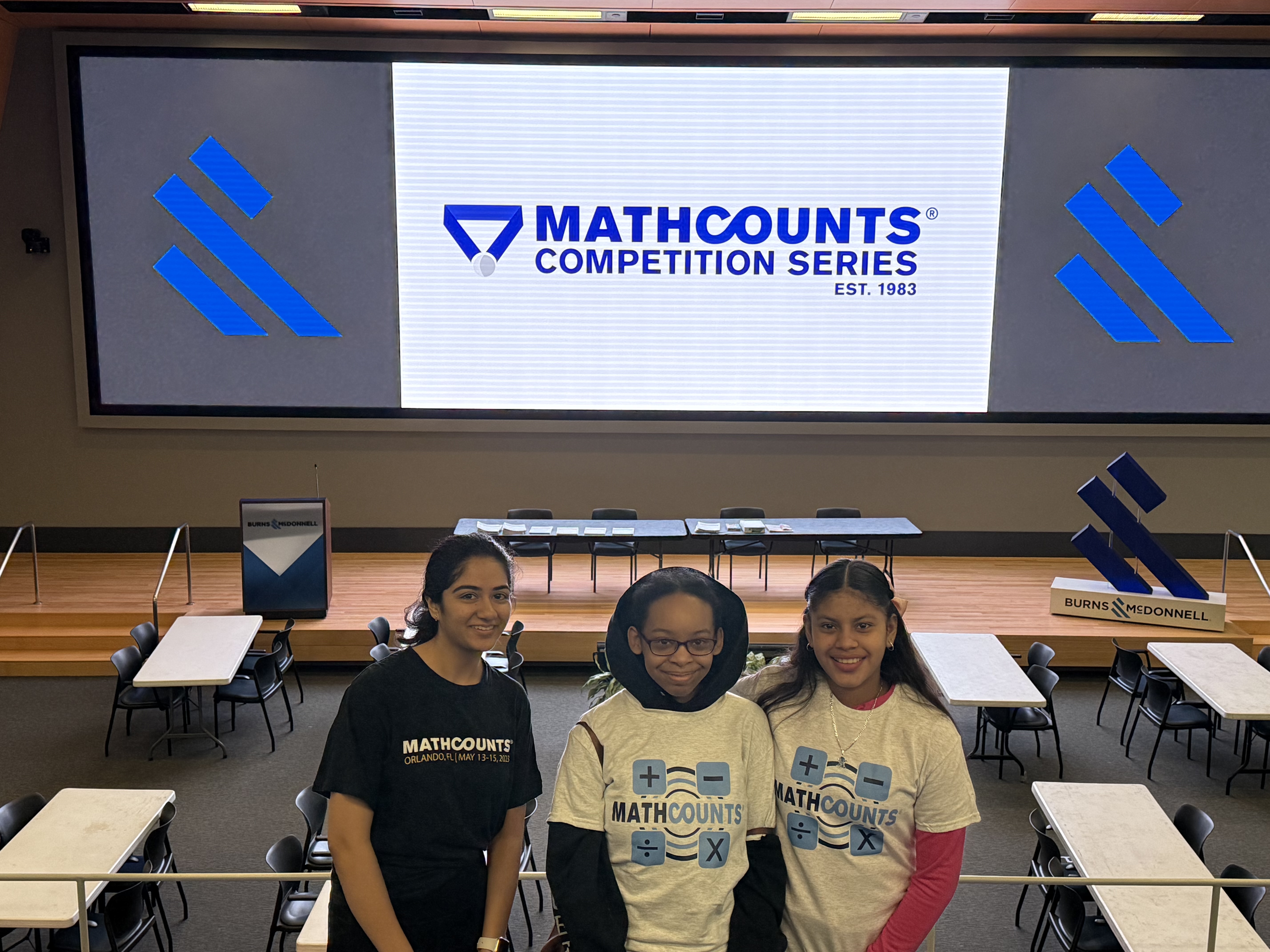 A high school student poses with two middle school students at a MATHCOUNTS competition