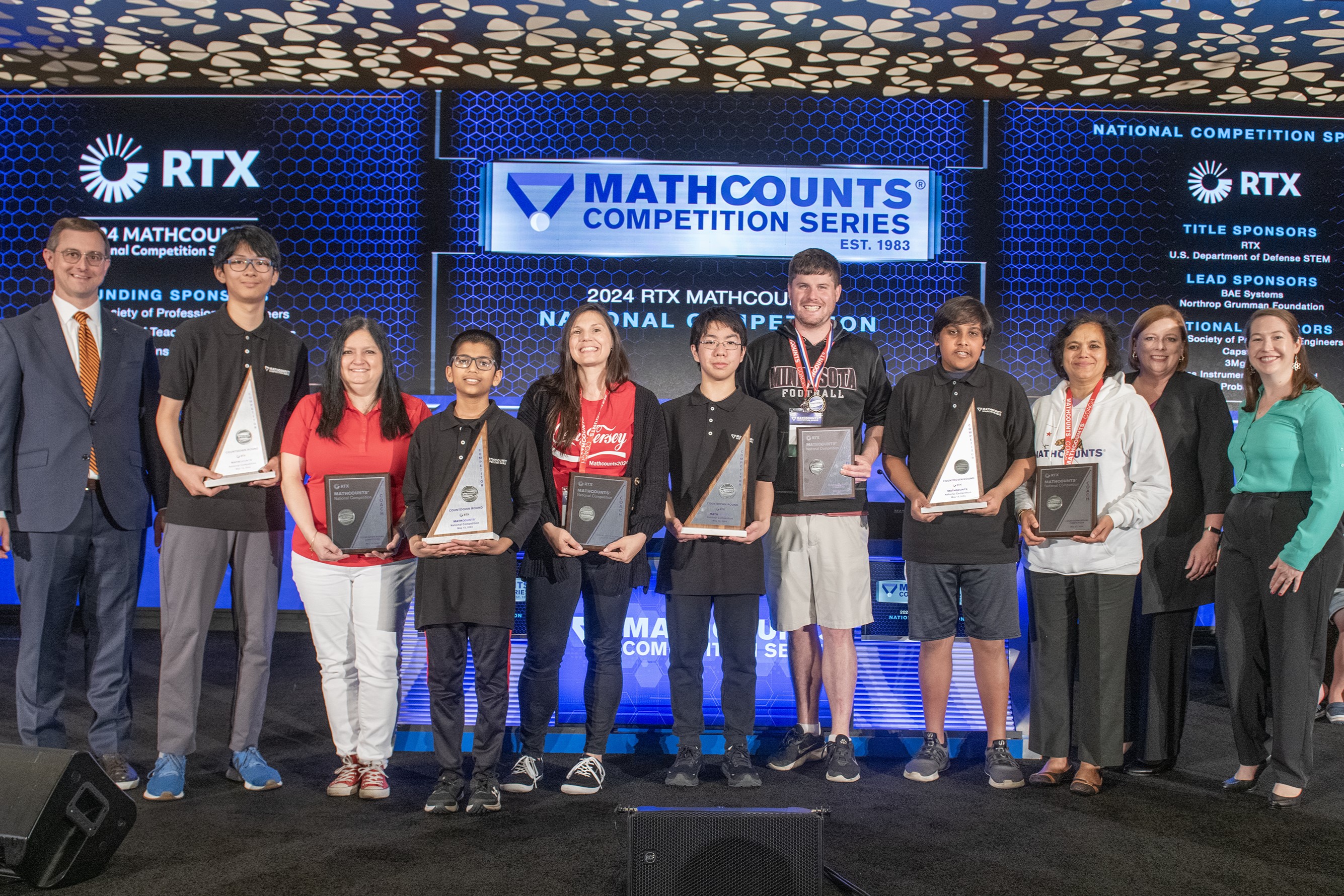 Participants hold their trophies onstage with their coaches