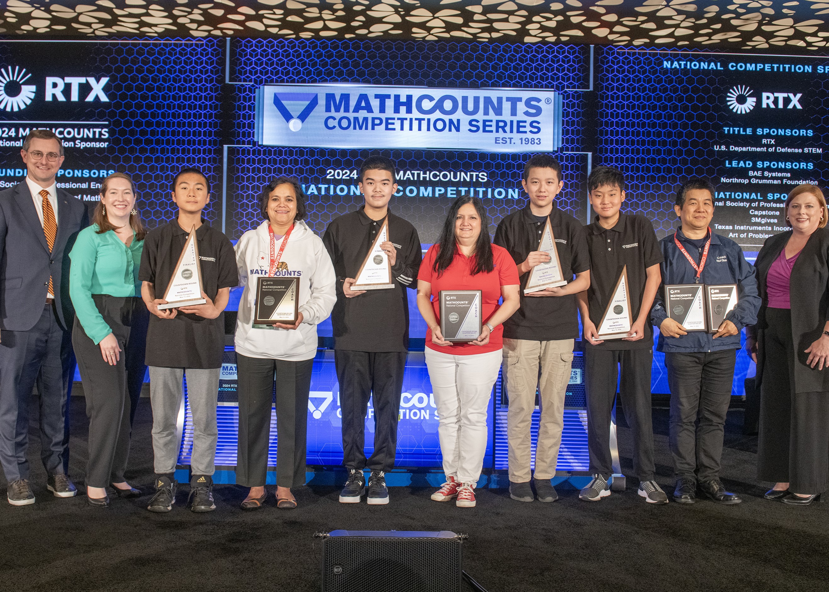 Quarterfinalists hold their trophies onstage with their coaches
